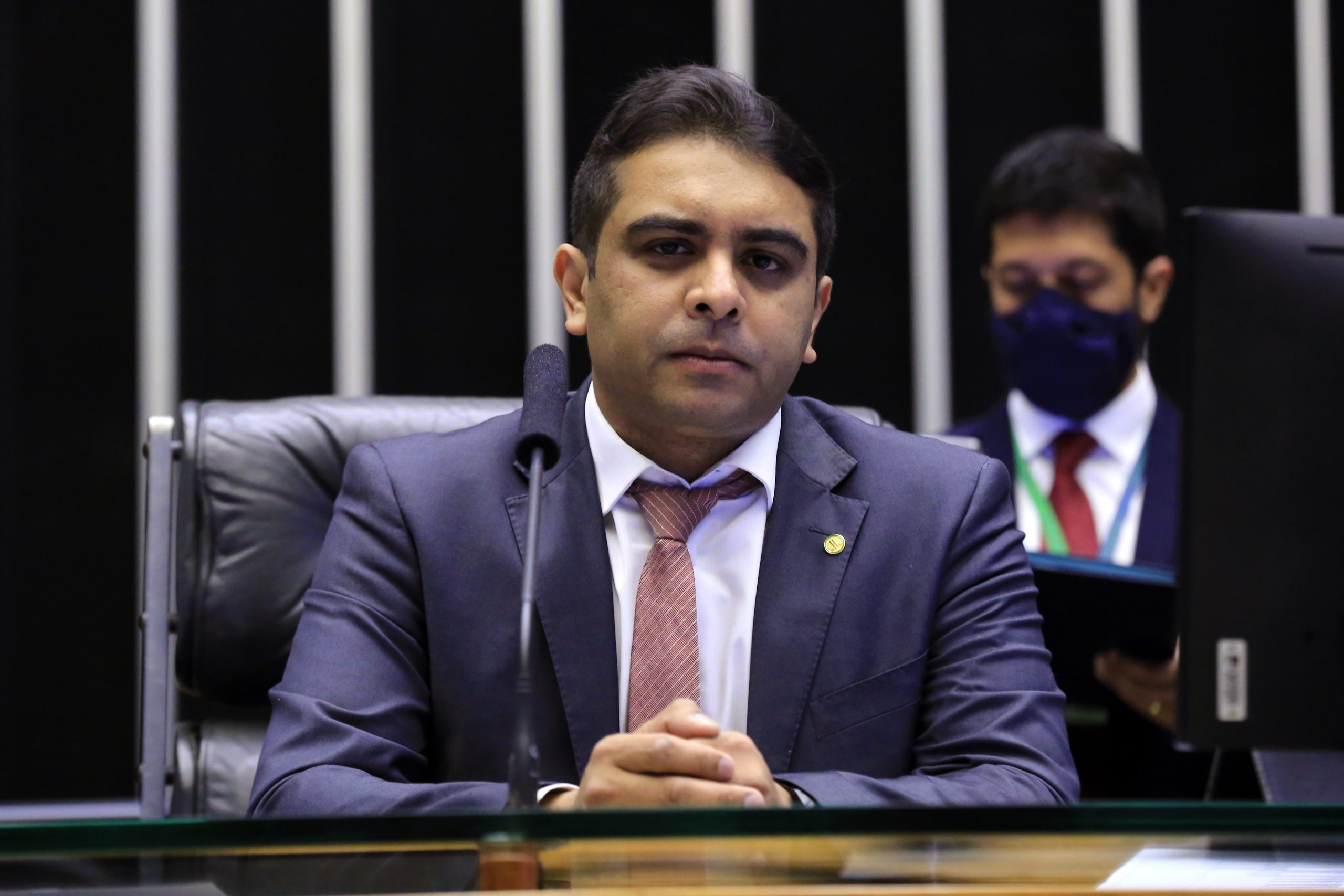 Deputado Fernando Rodolfo está sentado à mesa falando ao microfone